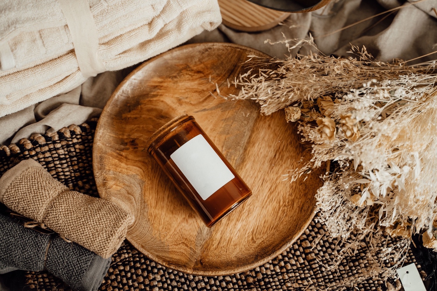 An amber candle, soft cream towels and dried botanicals on a wooden tray; illustrative stock photograph